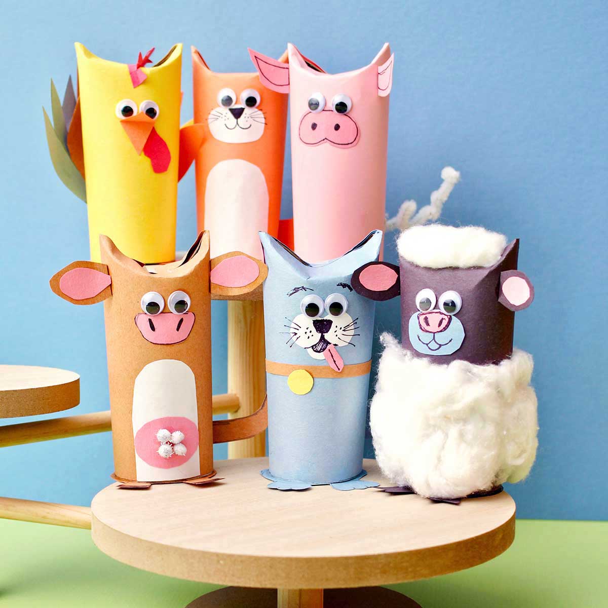 Six cute toilet paper roll animals on wooden stands in front of blue backdrop.