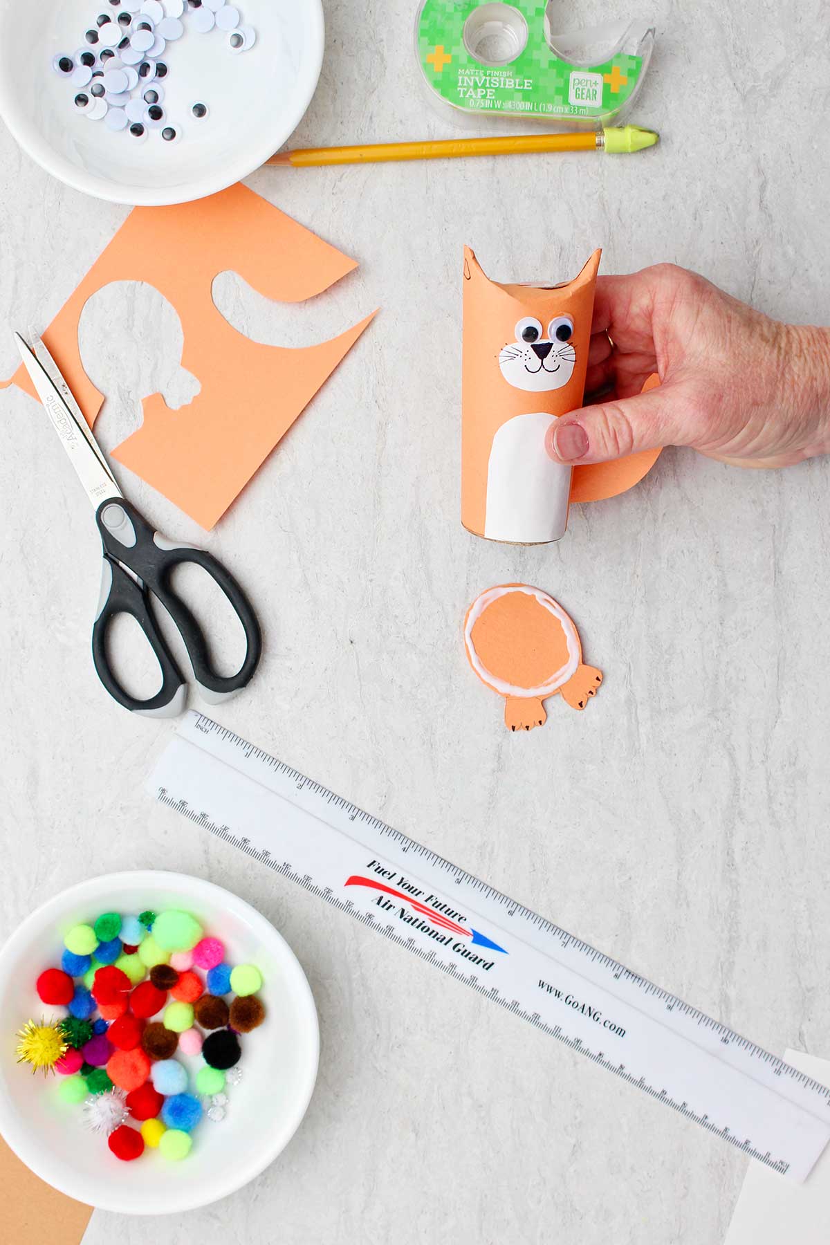 Hand holding cat toilet paper roll animal and showing how to glue the body to a base.