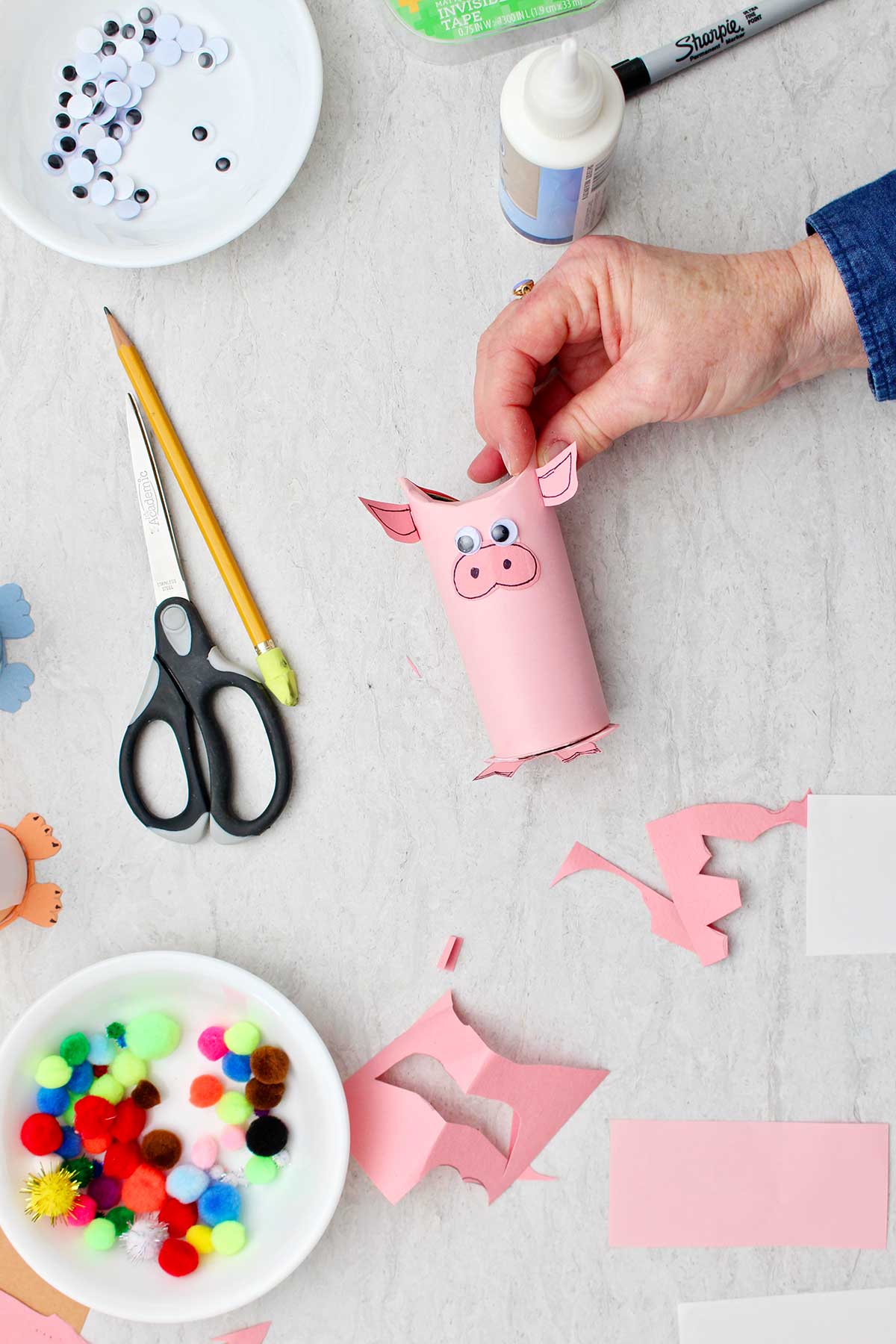 Hand adding pink ears to pig toilet paper roll animal.