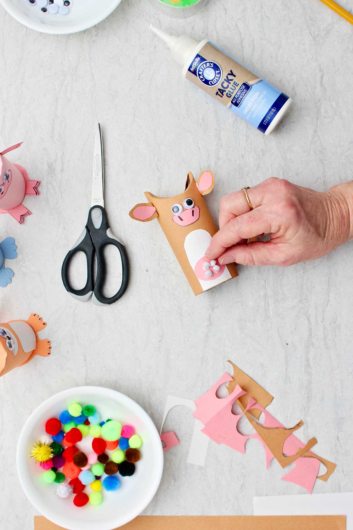 Hand adding white pom pom details to cow toilet paper roll animal.
