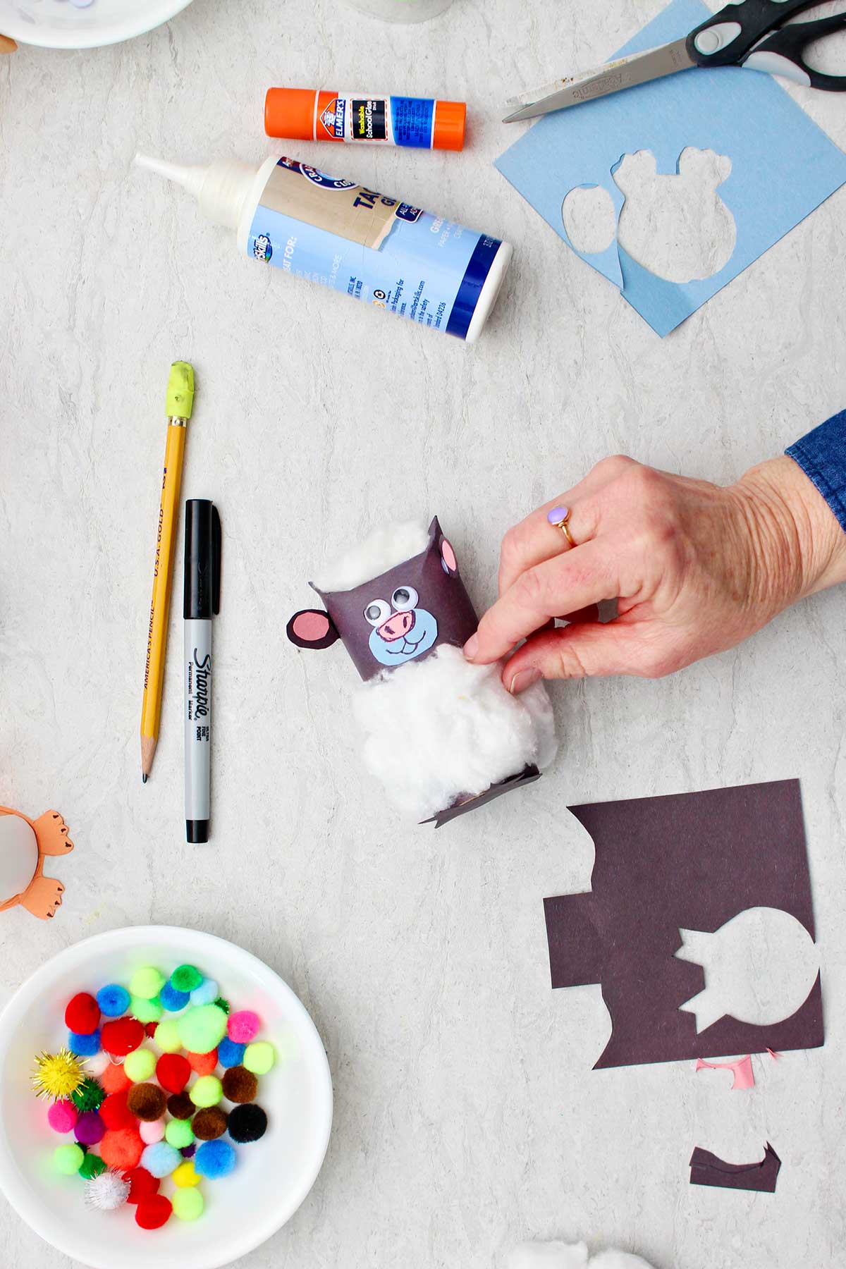 Hand adding cotton ball details to sheep toilet paper roll animal.