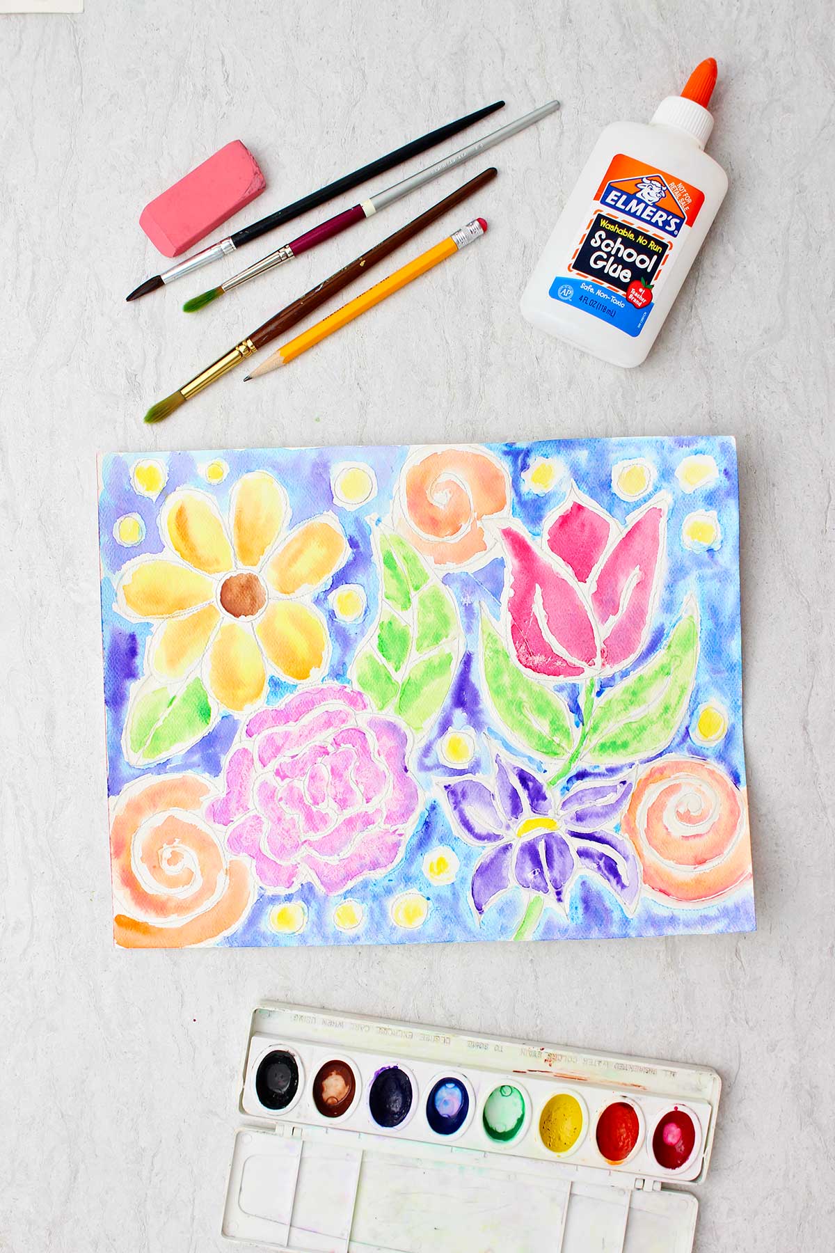 Completed glue line painting of colorful flowers with blue background with glue, brush, pencil, eraser and paints near by.