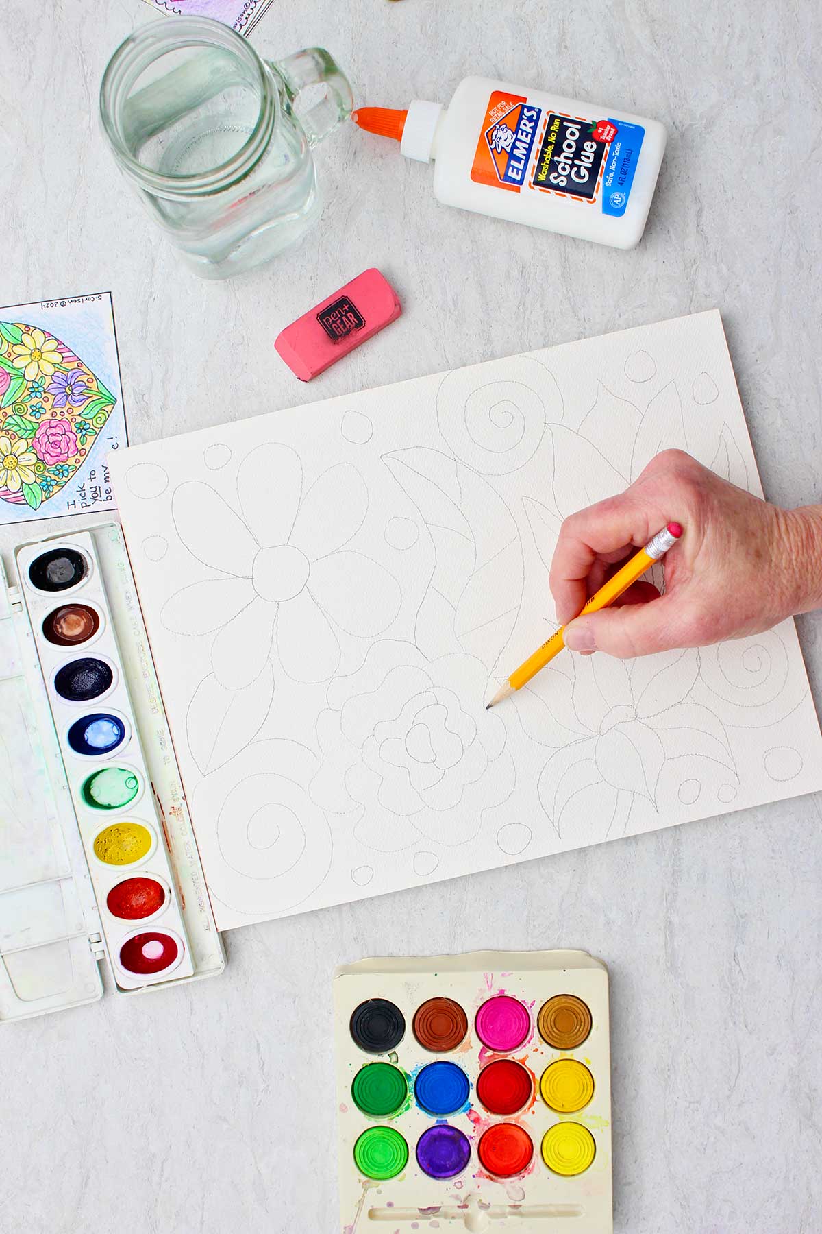 Hand sketching flowers on canvas with a pencil with supplies near by.
