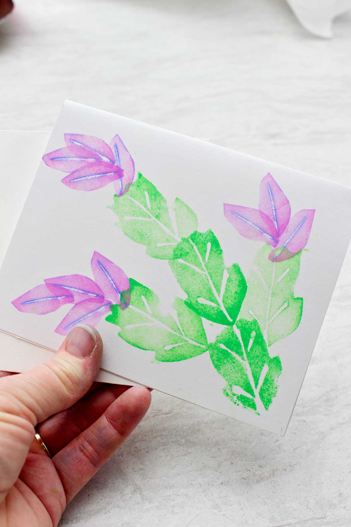 Hand holding print with leaves and purple flowers made from craft foam stamps.