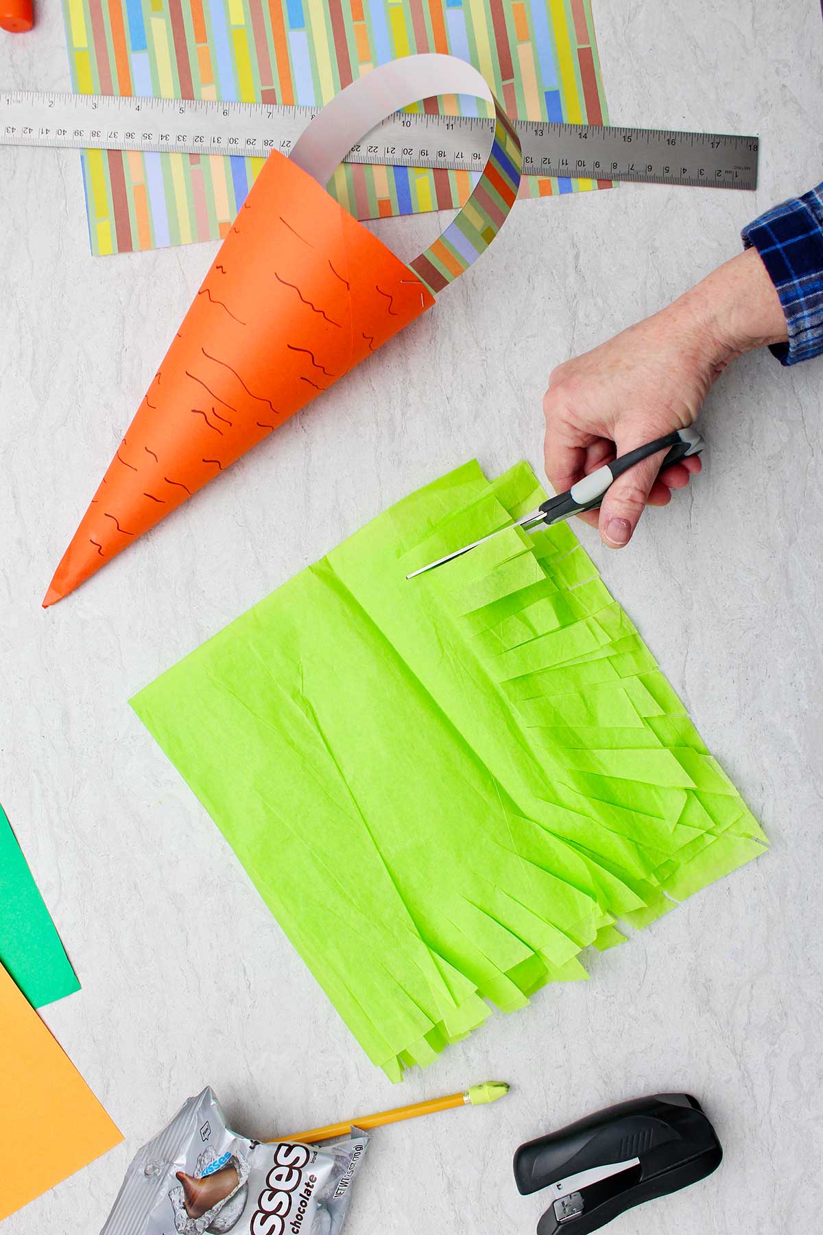 Hand cutting green tissue paper to make grass for carrot Easter basket.