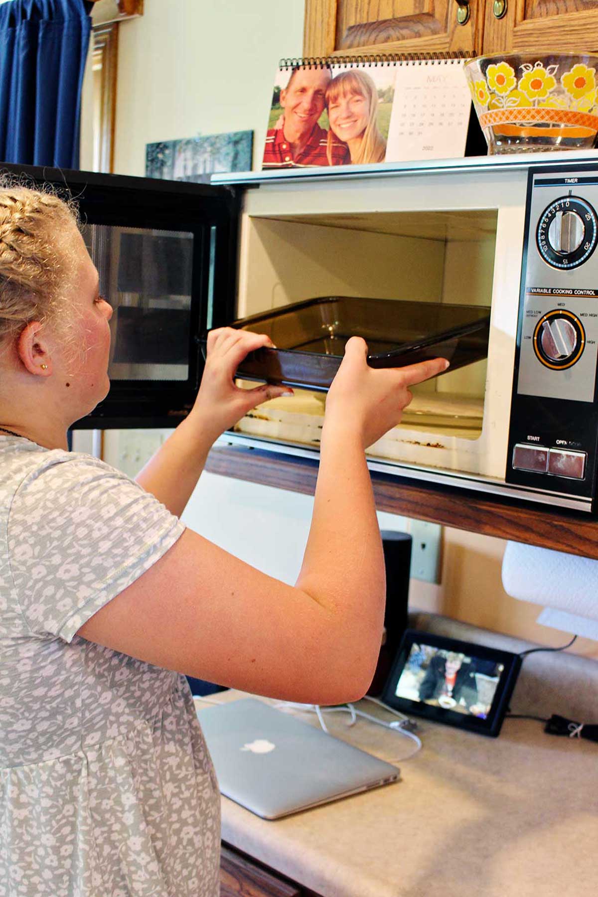 A girl placing a glass pan in a microwave.