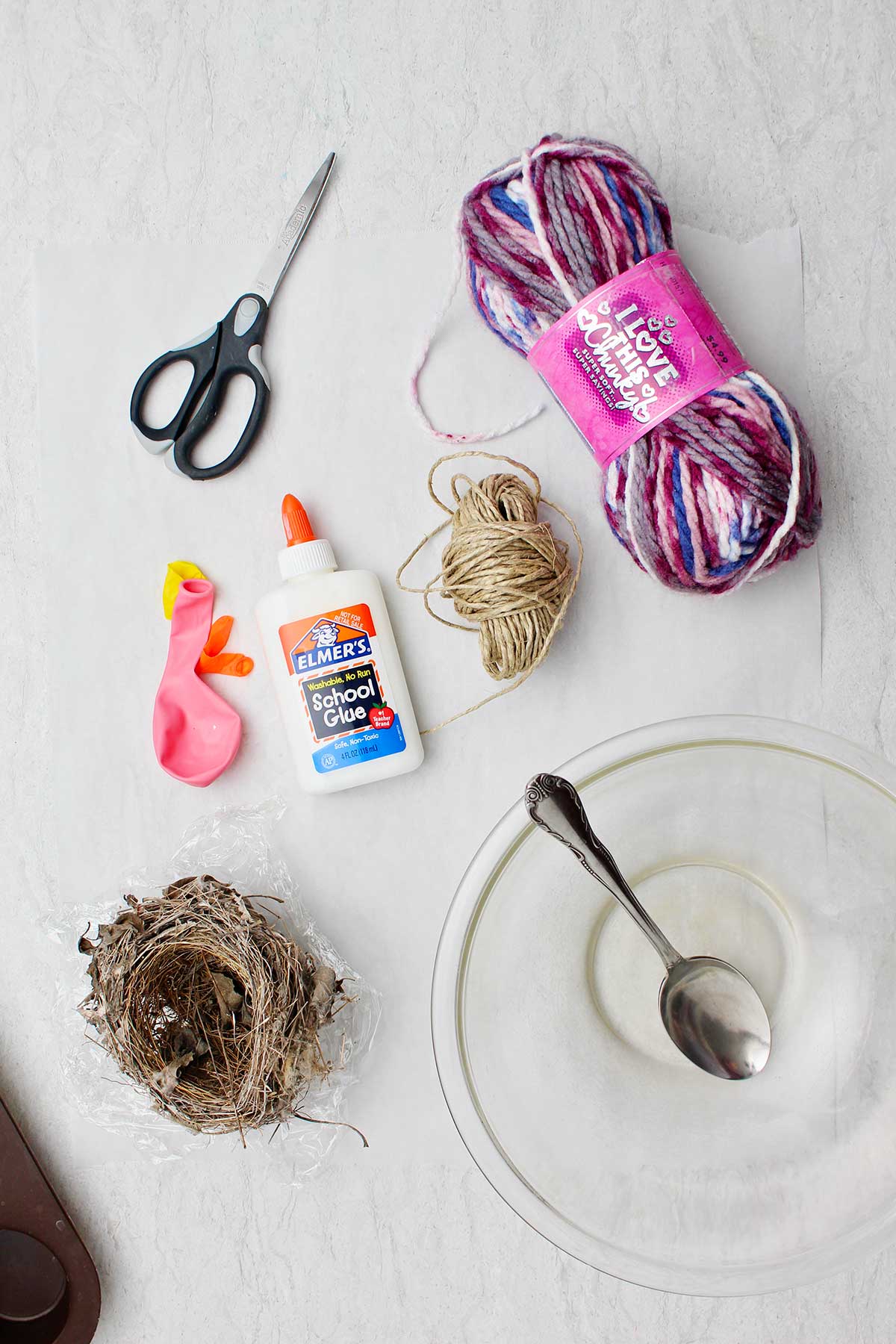 Supplies to make a bird nest out of string. Yarn, twine, a bowl, spoon, balloons, scissors and a real bird nest.