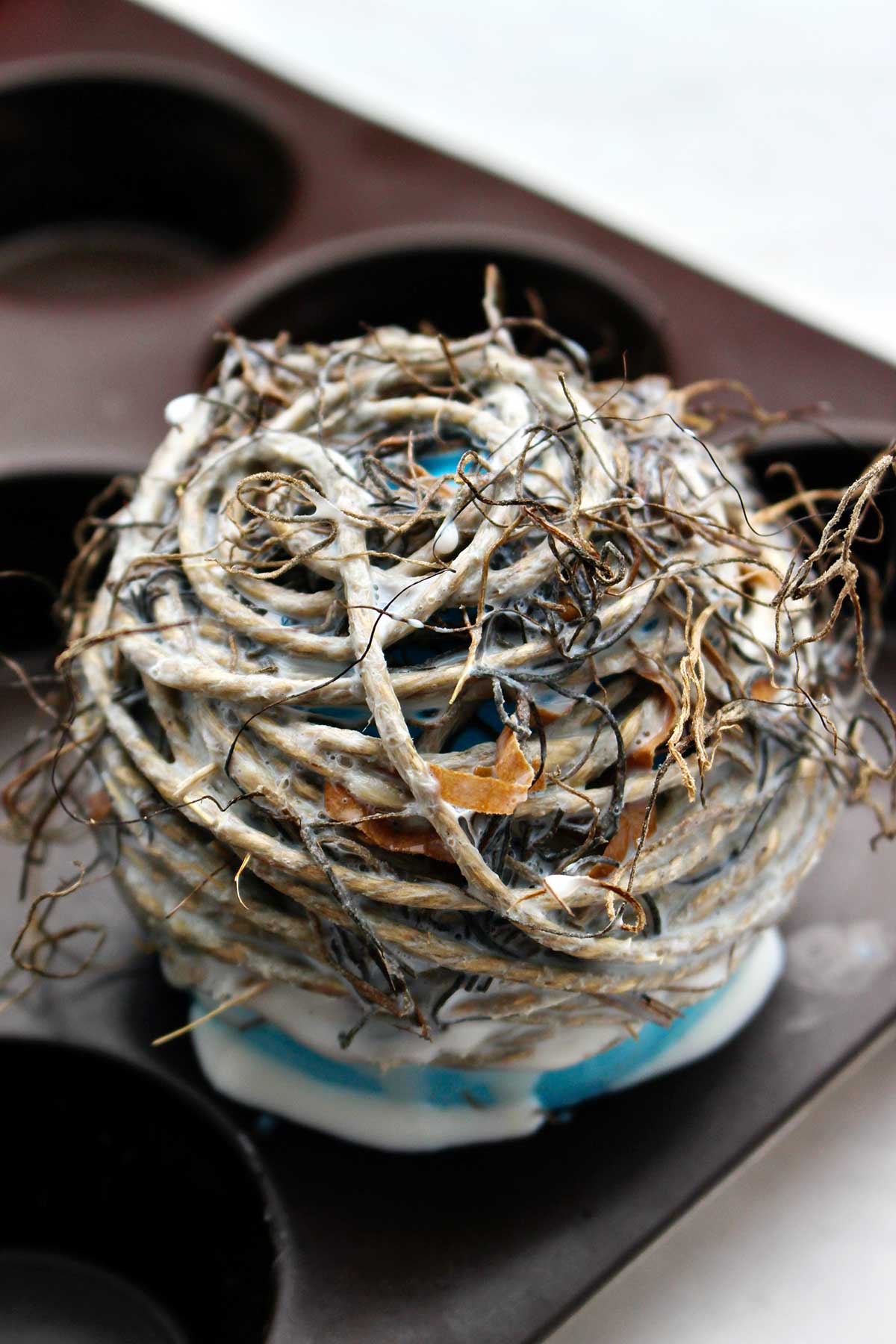 Inverted bird nest with balloon inside for shaping drying in a muffin tin.