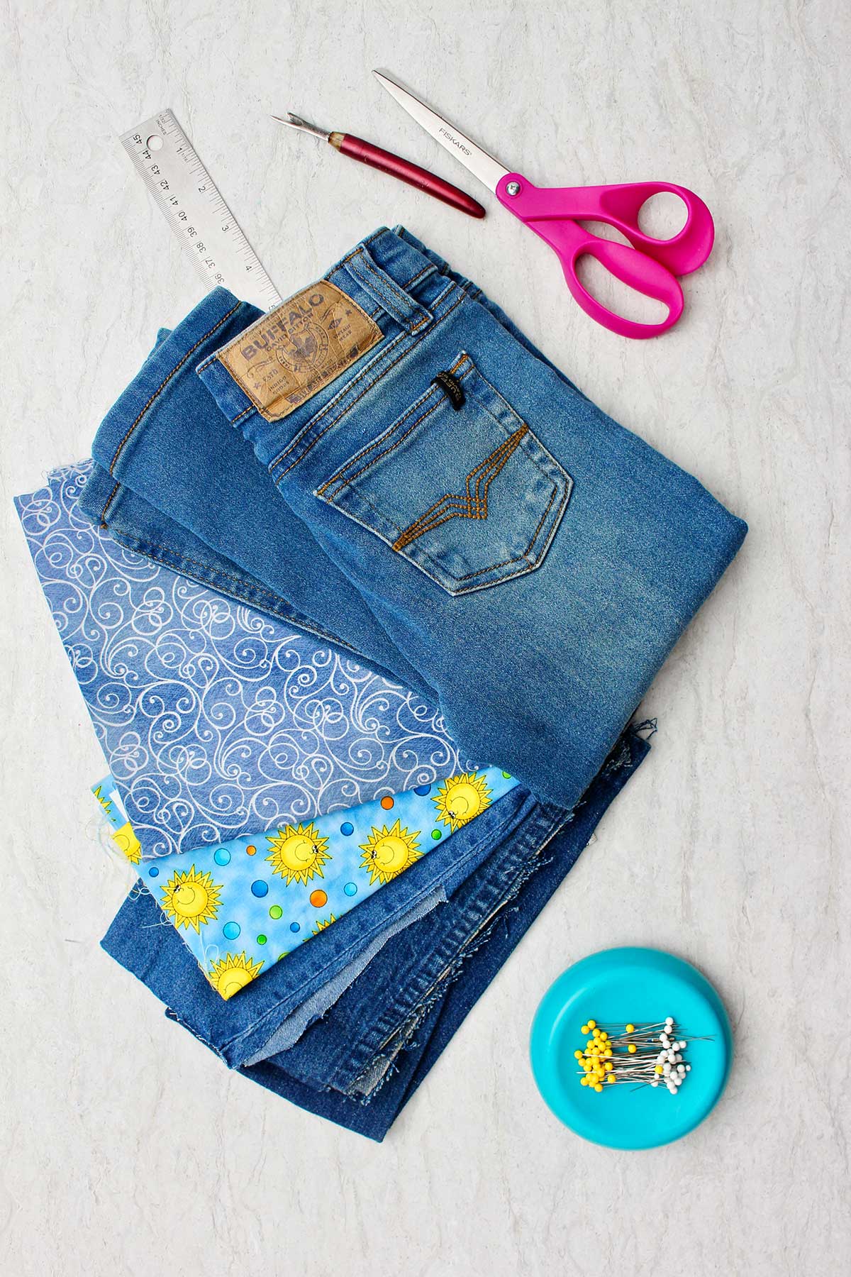 Supplies needed to make bell bottom jeans. A pair of jeans, scissors, decorative fabric, ruler and pins.