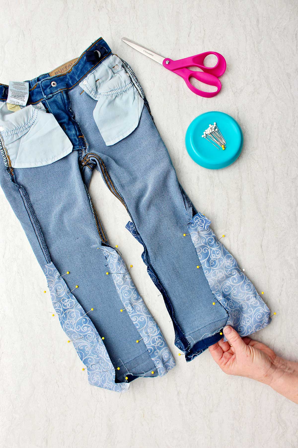 Inside out jeans with pins holding fabric in place to make bell bottoms with pins and scissors near by.