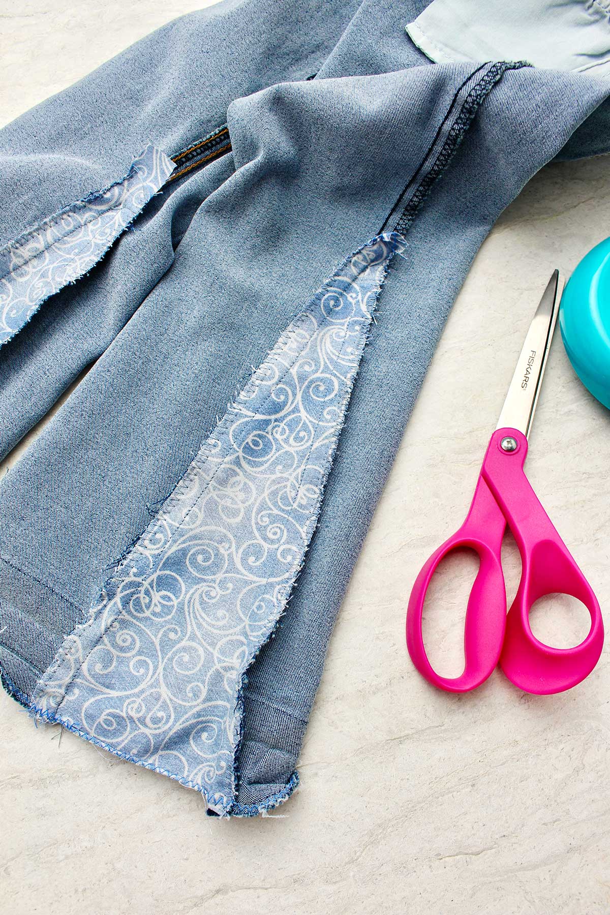 Close up view of inside out jeans with piece of fabric sewn in with scissors near by.