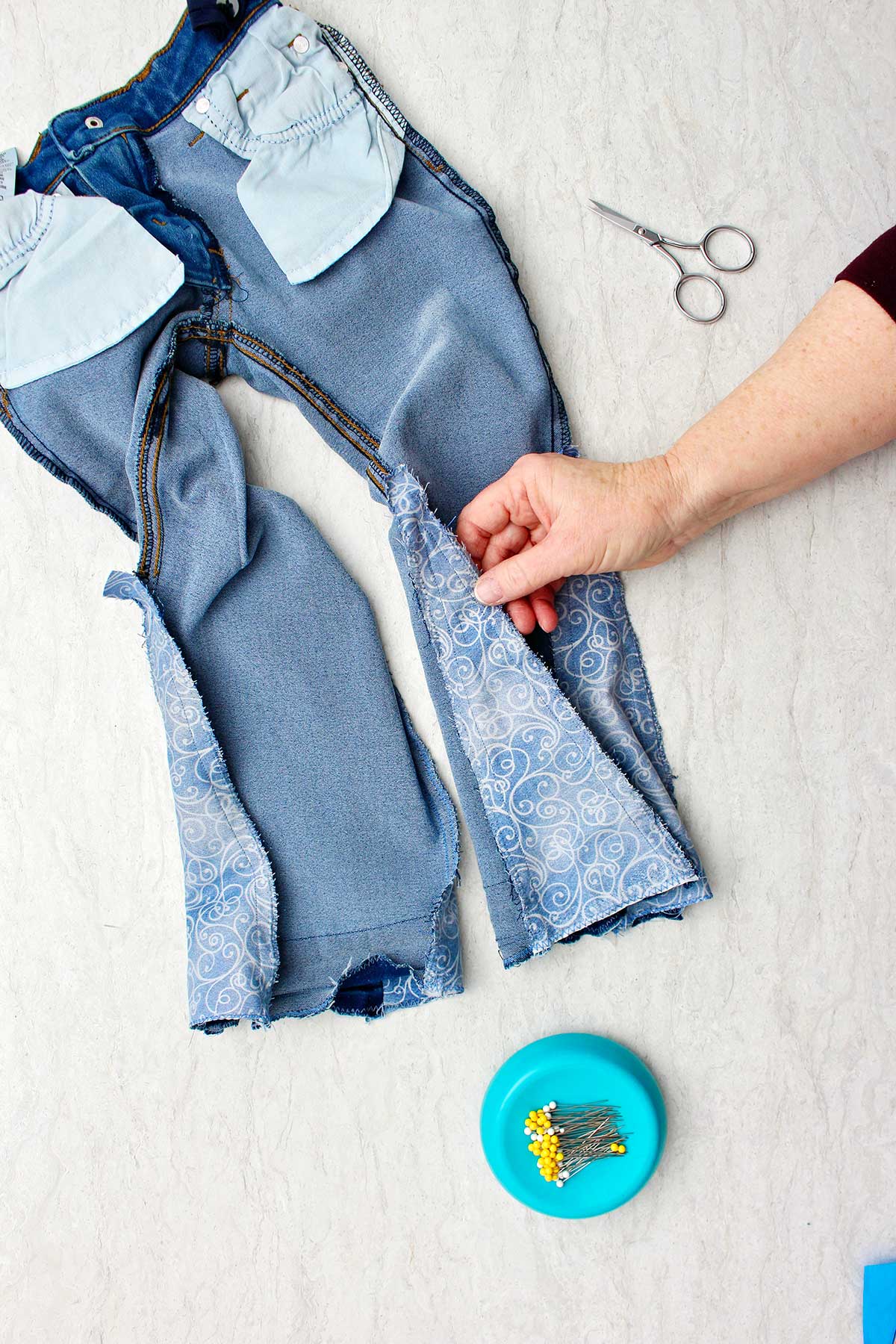 Hand showing inside out jeans with sewn in piece of fabric to make bell bottoms.