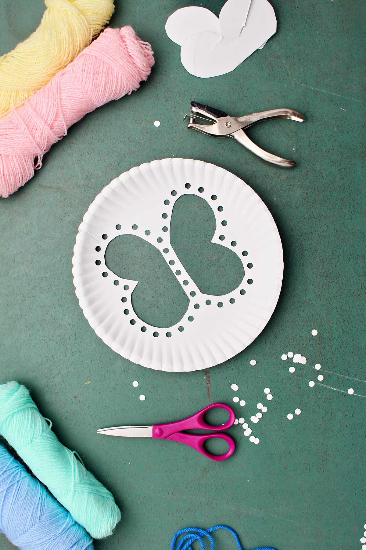 Paper plate with butterfly cut out with holes punched around the cut out with other supplies near by.