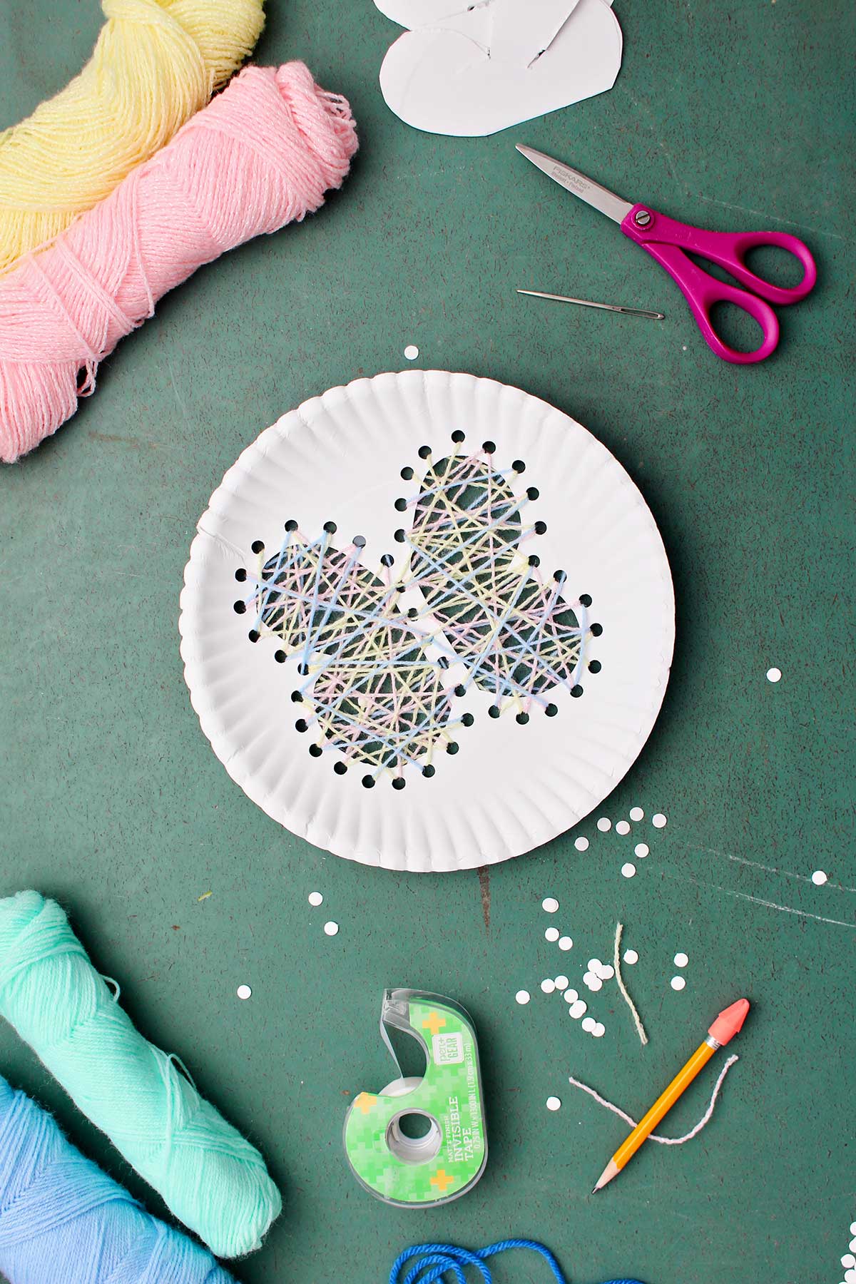 Paper plate string art of a butterfly with yarn and other supplies near by.