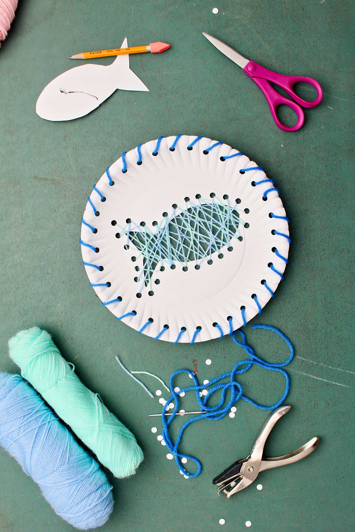 Fish design Paper Plate Sting Art made with blue yarn with supplies near by.