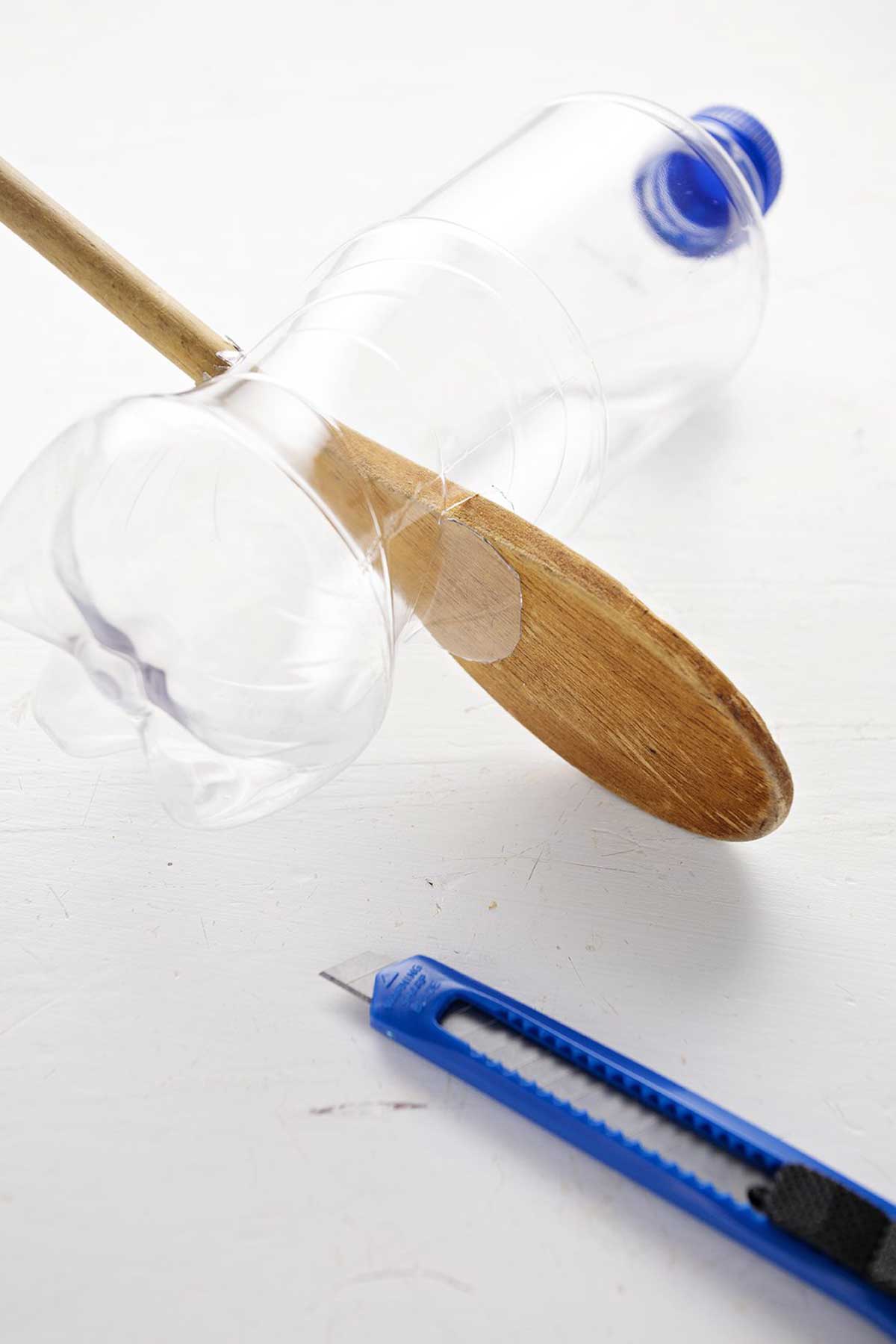 A plastic bottle with wooden spoons through it, and a utility knife.