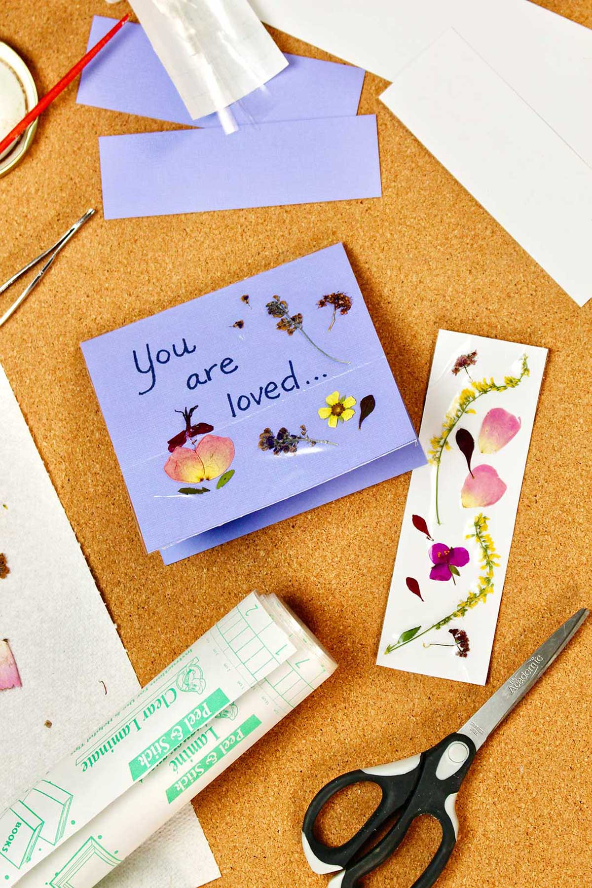 A purple card saying "You are loved..." with pressed flowers on it as well as a bookmark with pressed flowers.