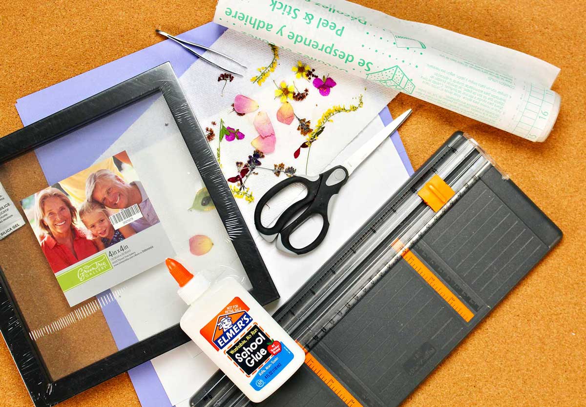 Supplies for pressed flower projects. Paper cutter, white glue, scissors, pressed flowers and picture frame.
