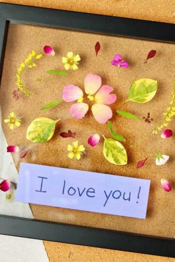 Framed pressed flowers with a purple tag inside saying "I love you!"