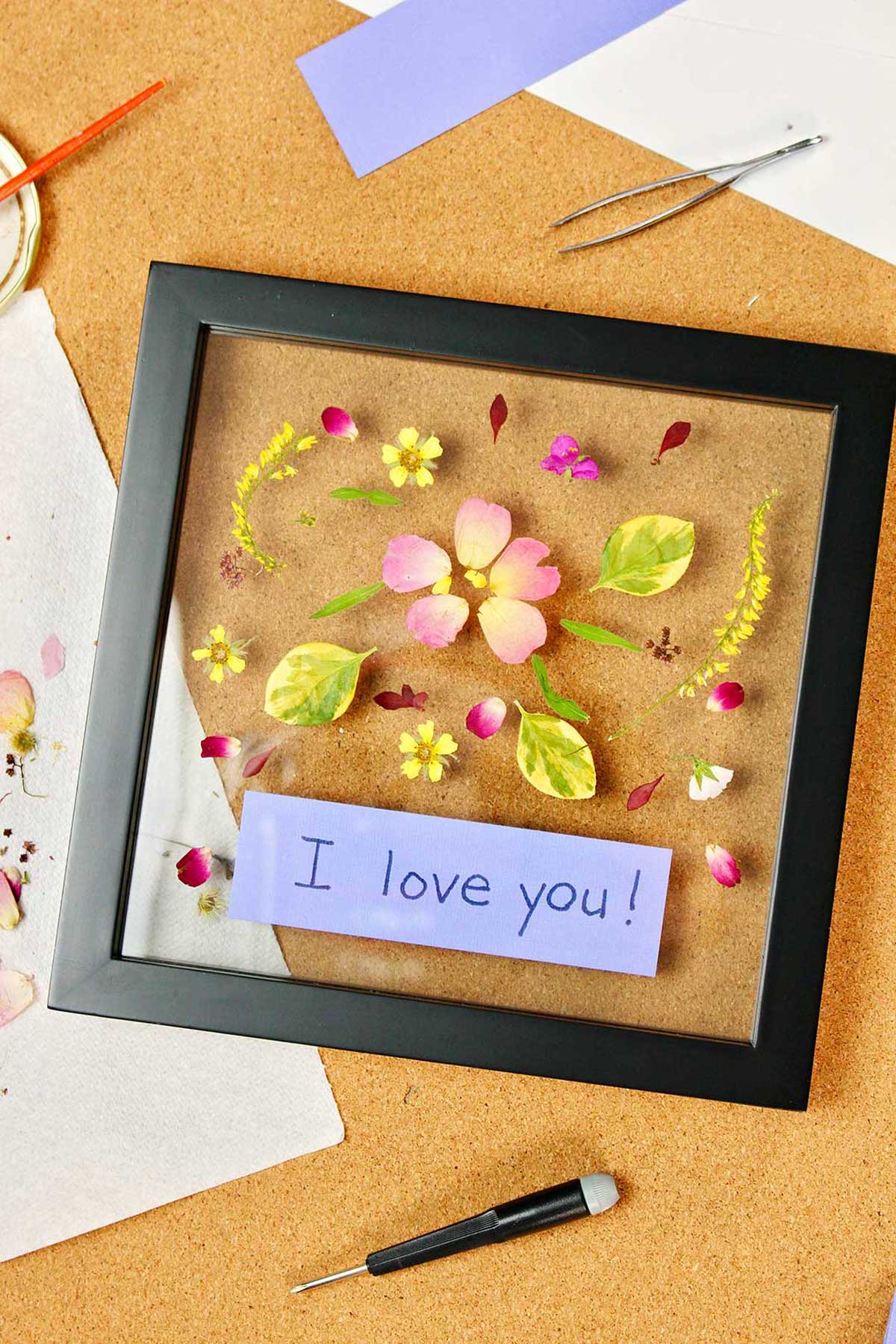 Framed pressed flowers with a purple tag inside saying "I love you!"