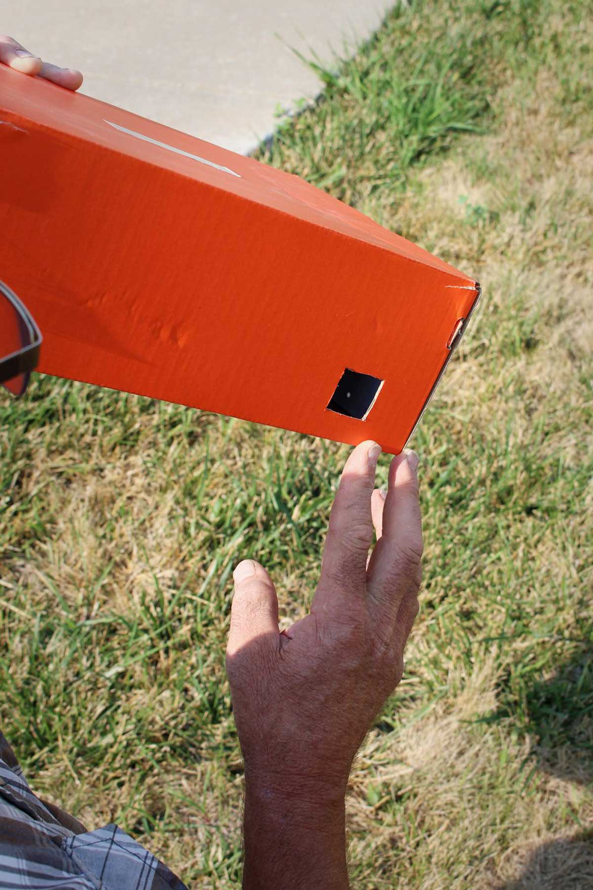 A man looking through a Solar Eclipse Pinhole Projector made from a recycled shoe box.