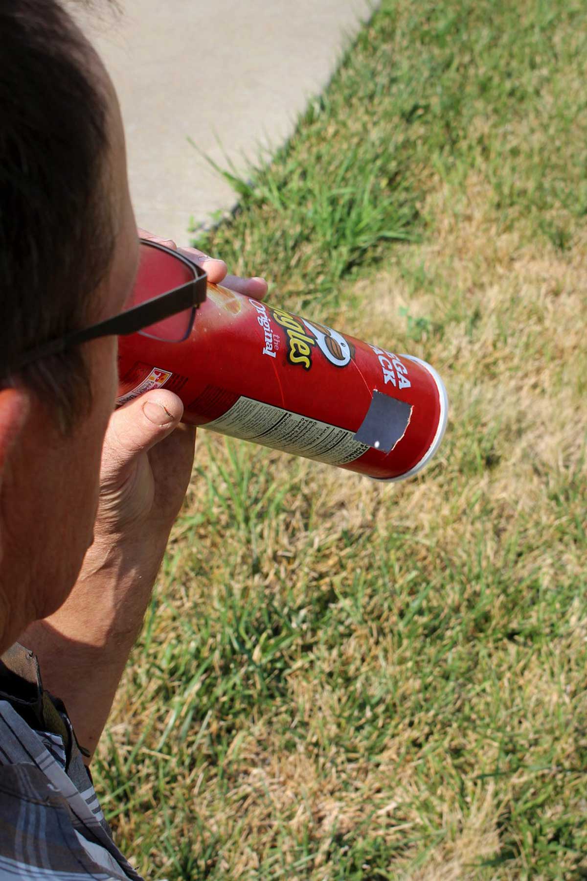 A man looking through a Solar Eclipse Pinhole Projector made from a recycled Pringles can.