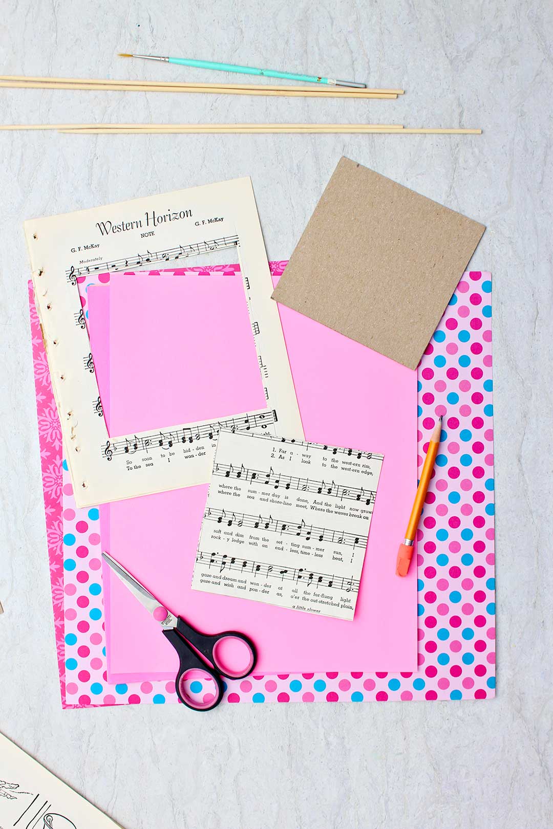 A piece of sheet music cut into a square rests on top of a stack of pink scrapbook paper.