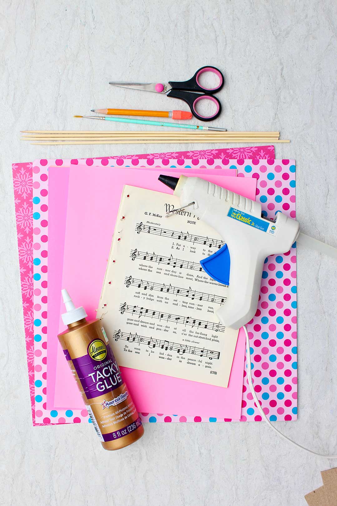 Supplies for making Book Page Roses. Sheet music, hot glue gun, wooden dowels, Tacky Glue, scissors and scrapbook paper.