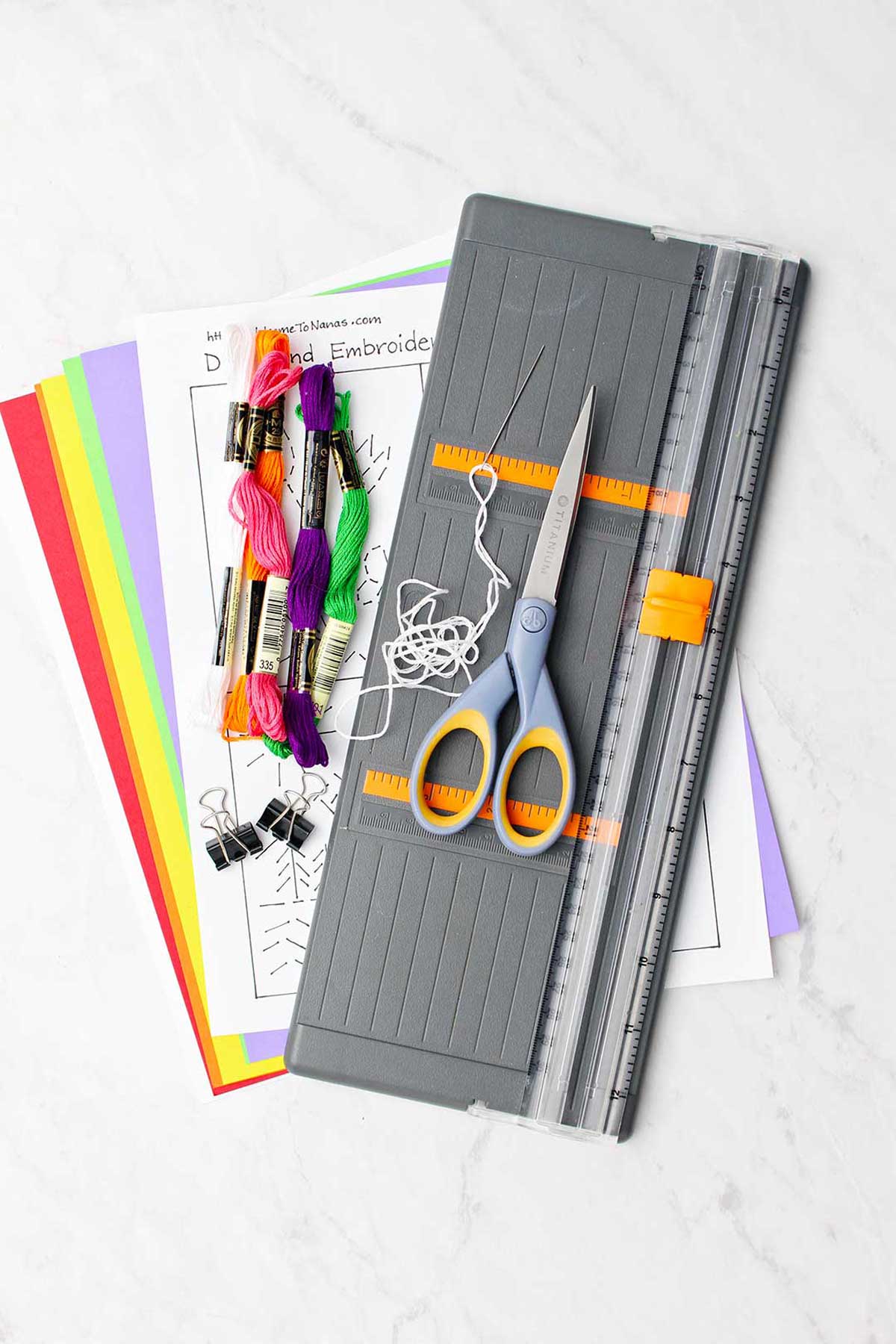 Supplies for hand embroidered card. Colorful embroidery floss, paper, templates, scissors and paper cutter.