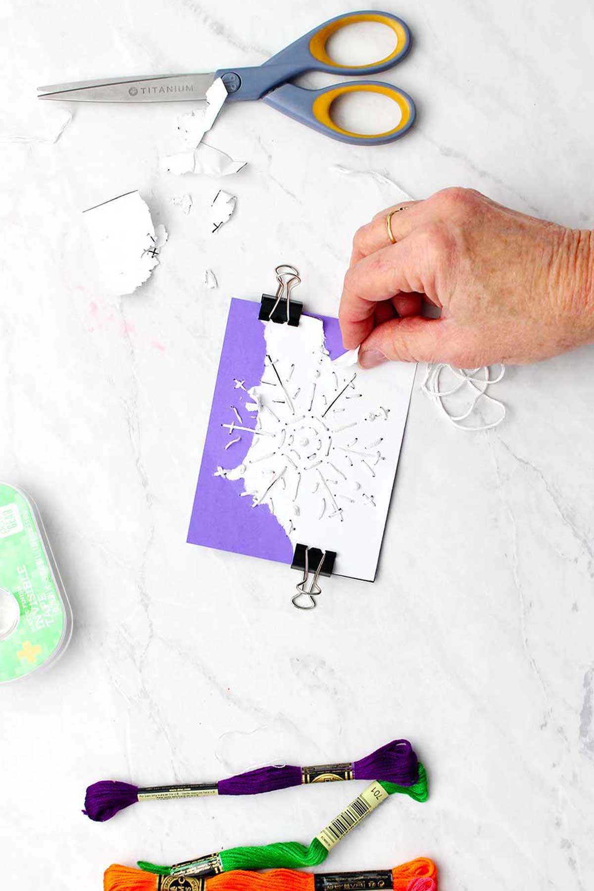 Hand ripping off the white paper snowflake template from the purple card.