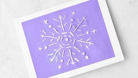 Completed snowflake embroidered greeting card with embroidery floss, glue and scissors nearby.
