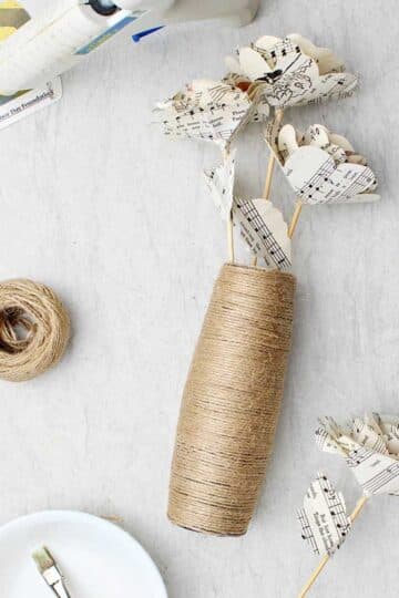 Twine wrapped vase laying down on a marble counter top with paper flowers inside.