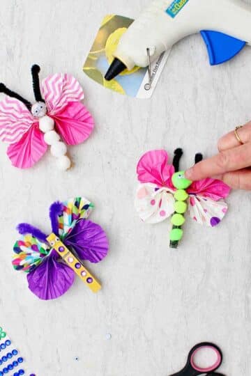 Hand securing a googly eye on Easy Butterfly Clothespin with two other completed ones near by.