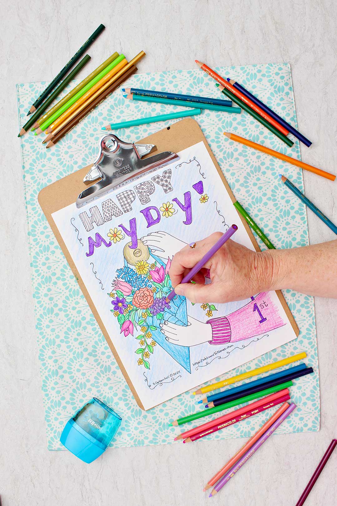 A May Day coloring page on a clip board being colored with coloring pencils