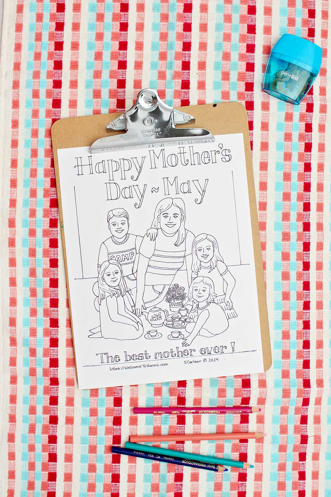 Uncolored Mother's Day Coloring Page attached to clipboard on red, coral and aqua towel with colored pencils near by.
