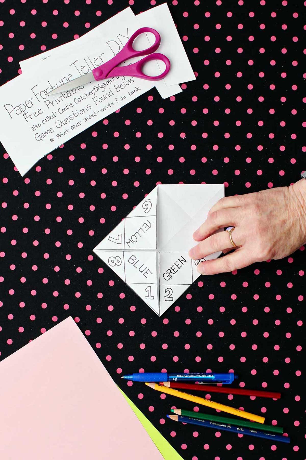 White printable fortune teller with one flap flipped open resting on black and pink polka dotted background.