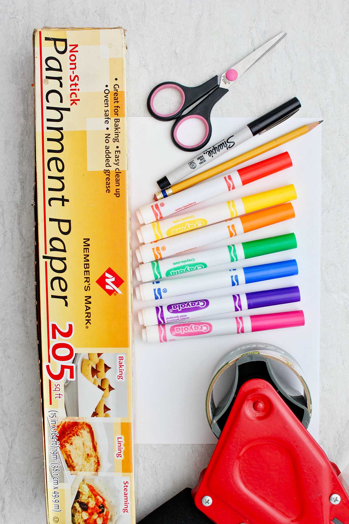 Markers, sharpie, pencil, paper, parchment paper, scissors and red packing tape dispenser.