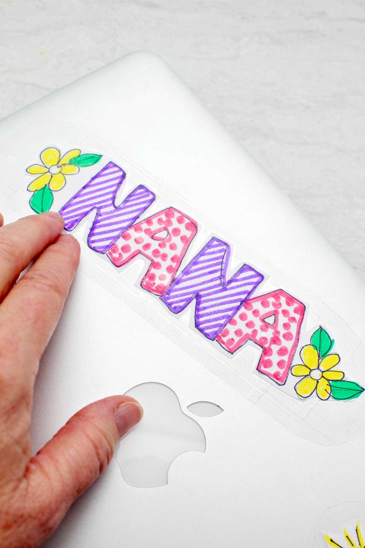 "NANA" sticker with yellow flowers being stuck to a silver laptop.