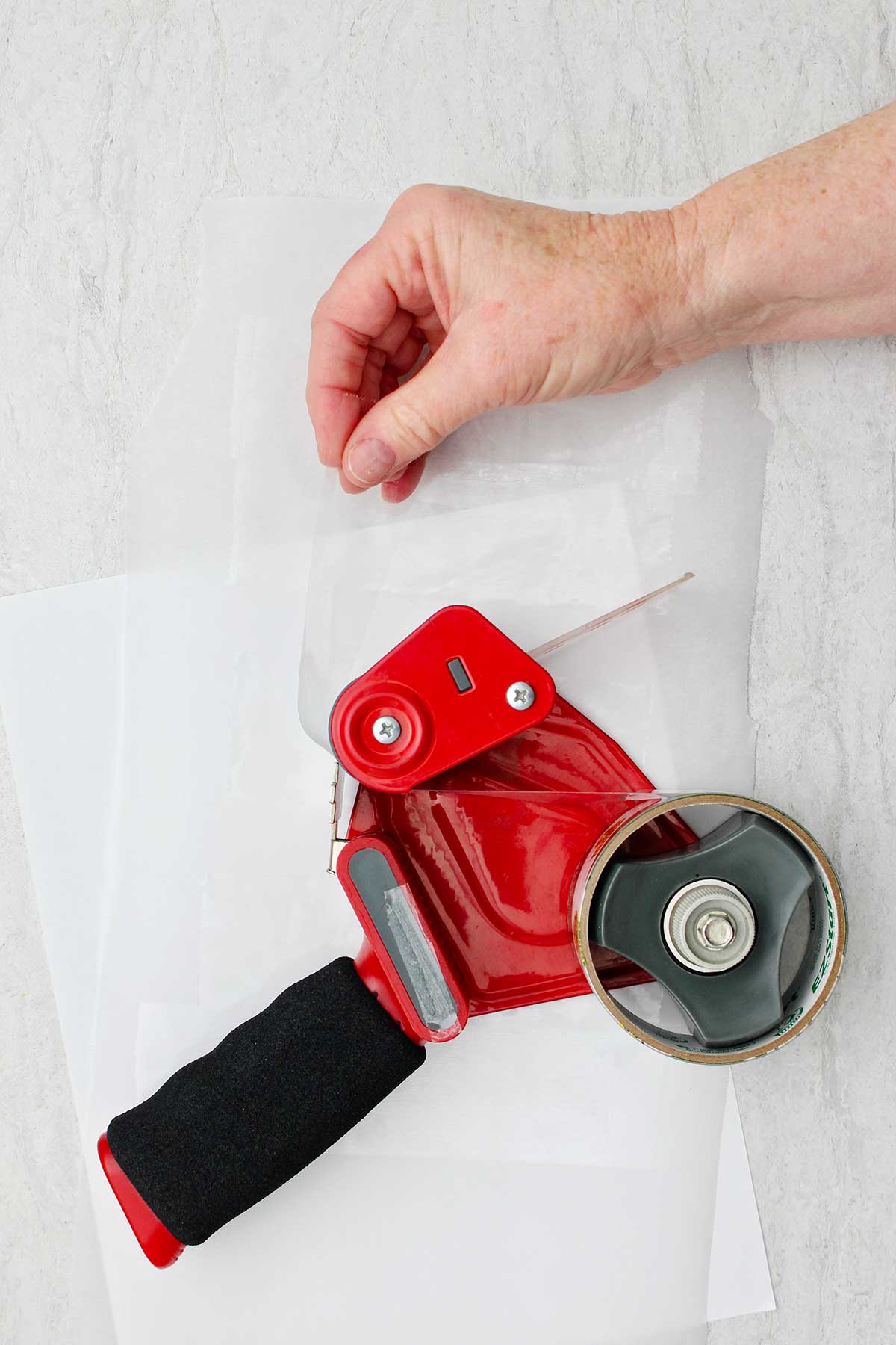 Hand removing piece of tape from a red packing tap dispenser.