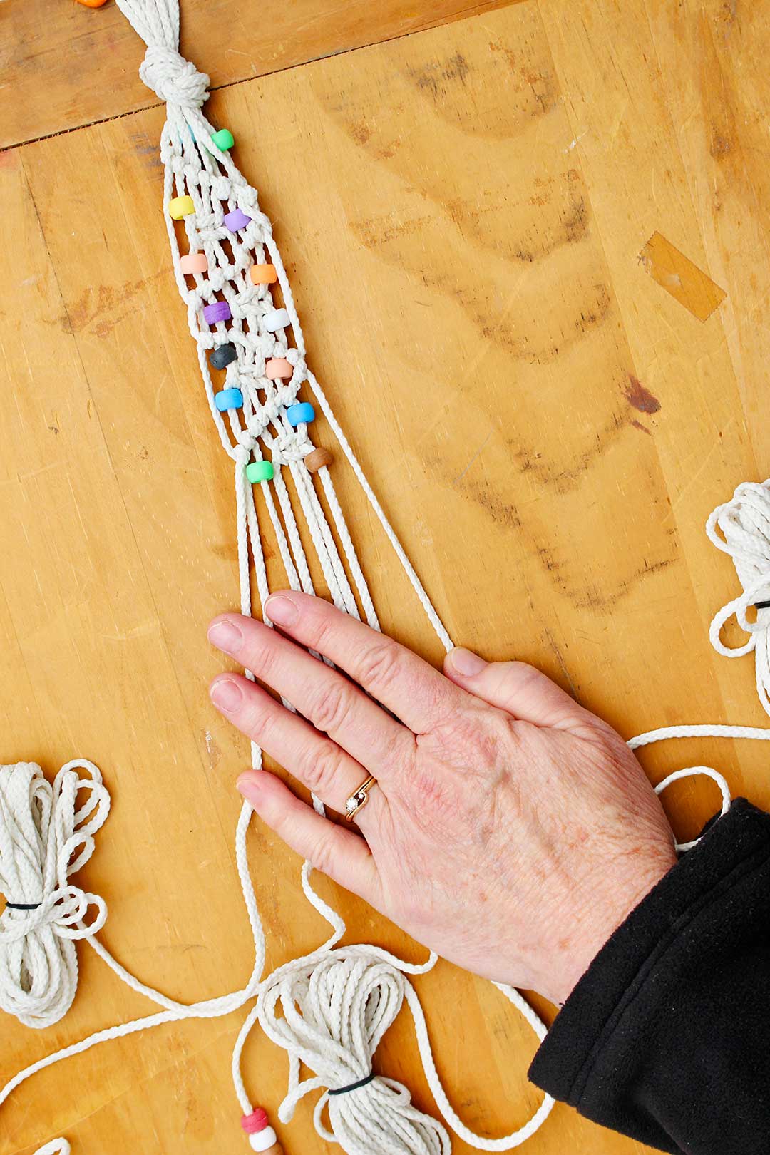 Hand holding cords while making a macrame belt with beads.