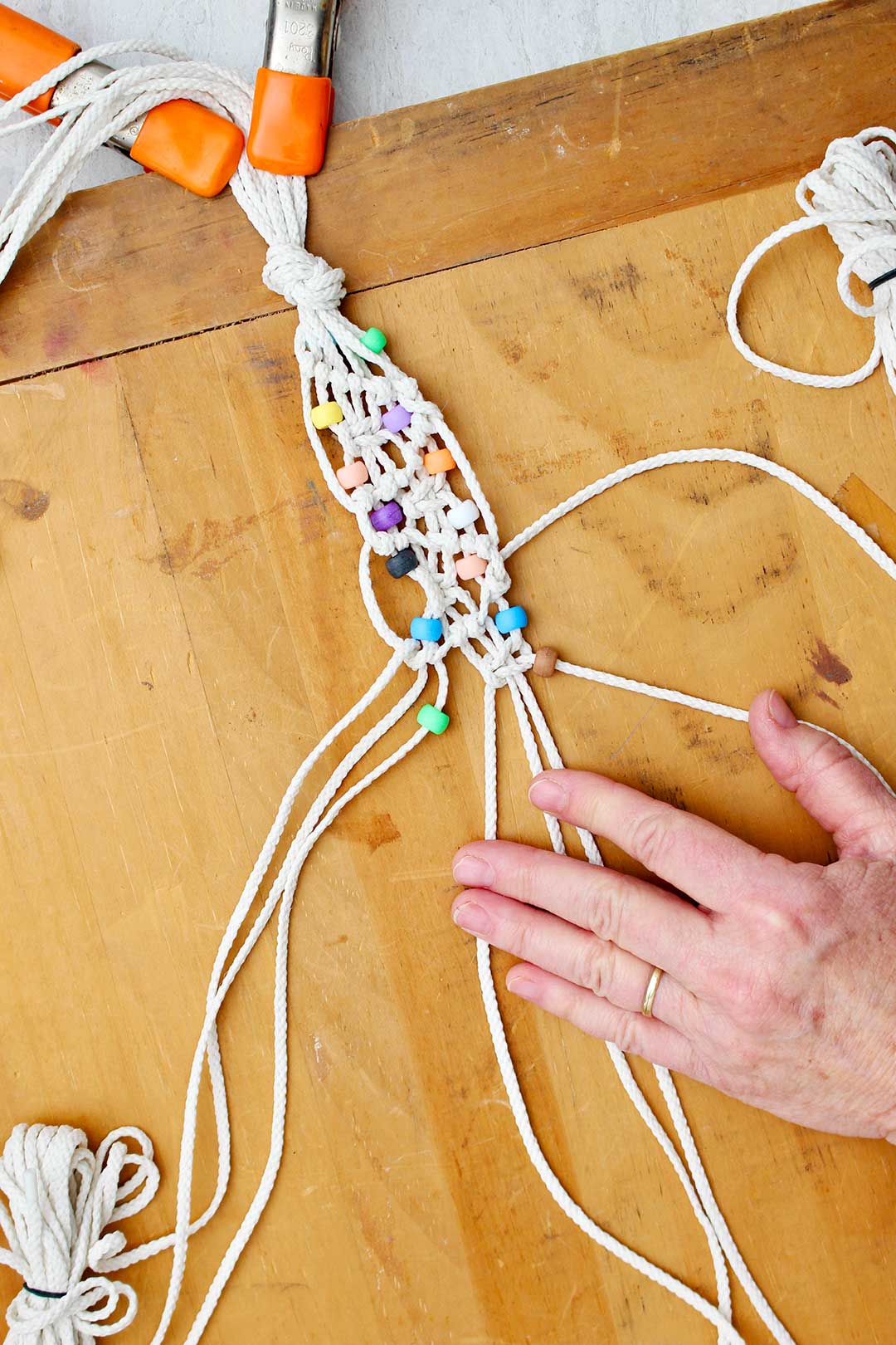 Hand holding cords while making a macrame belt with beads.