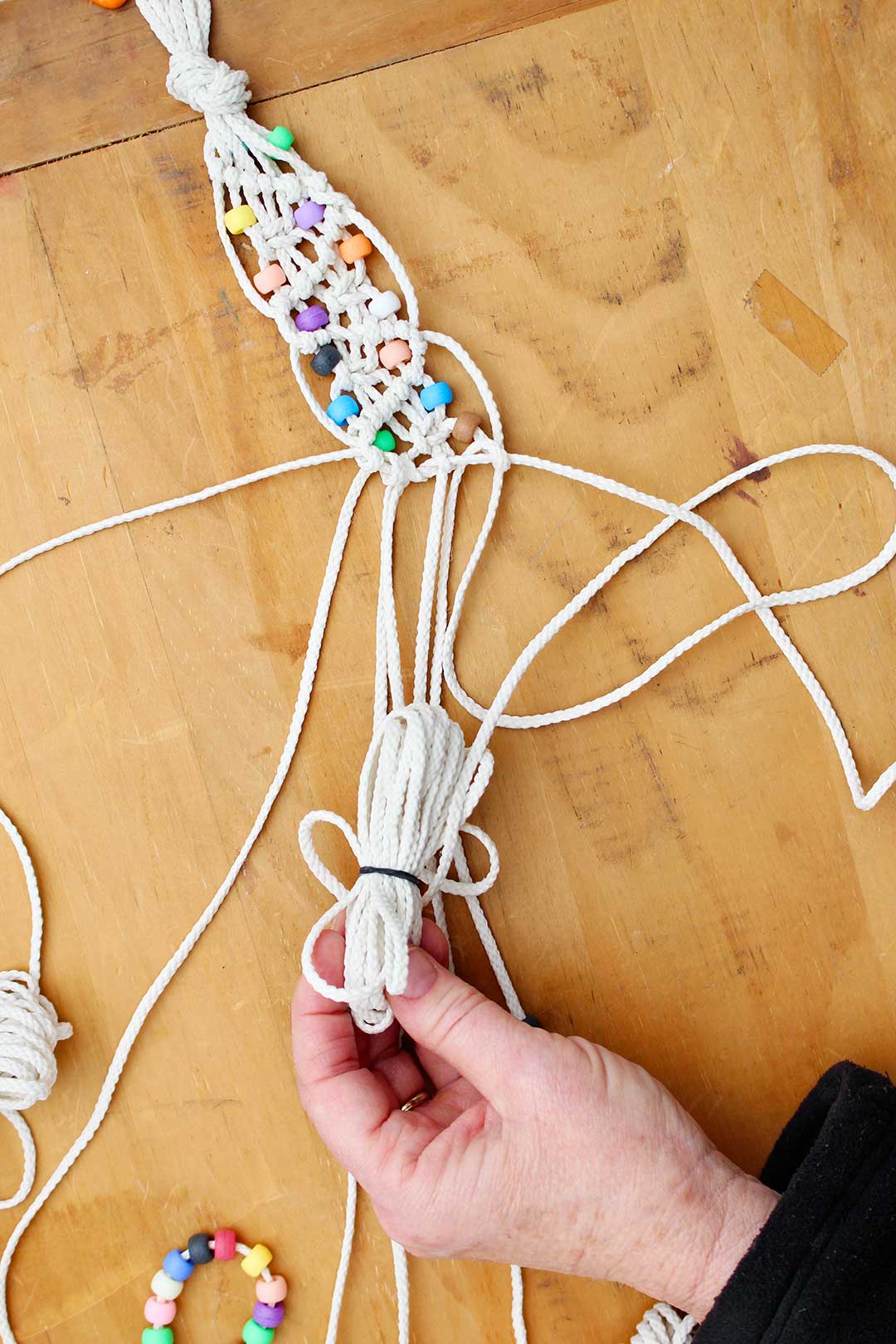 Hand holding cords while making a macrame belt with beads.