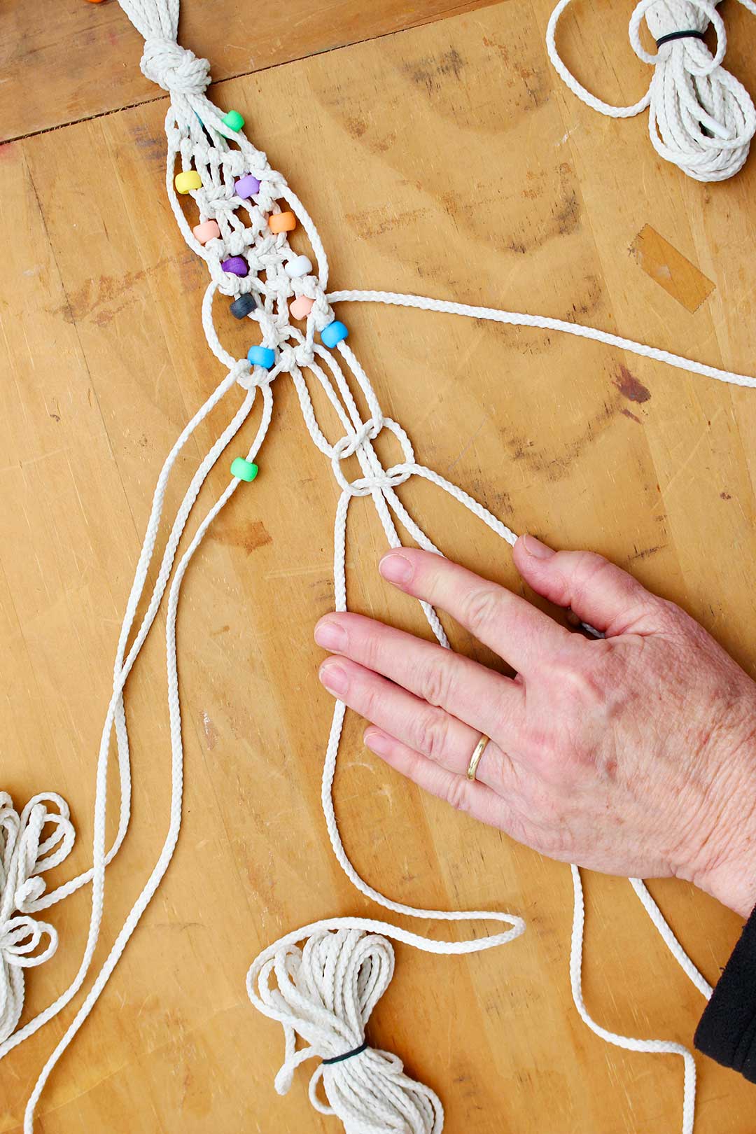 Hand holding cords while making a macrame knot on a belt with beads.