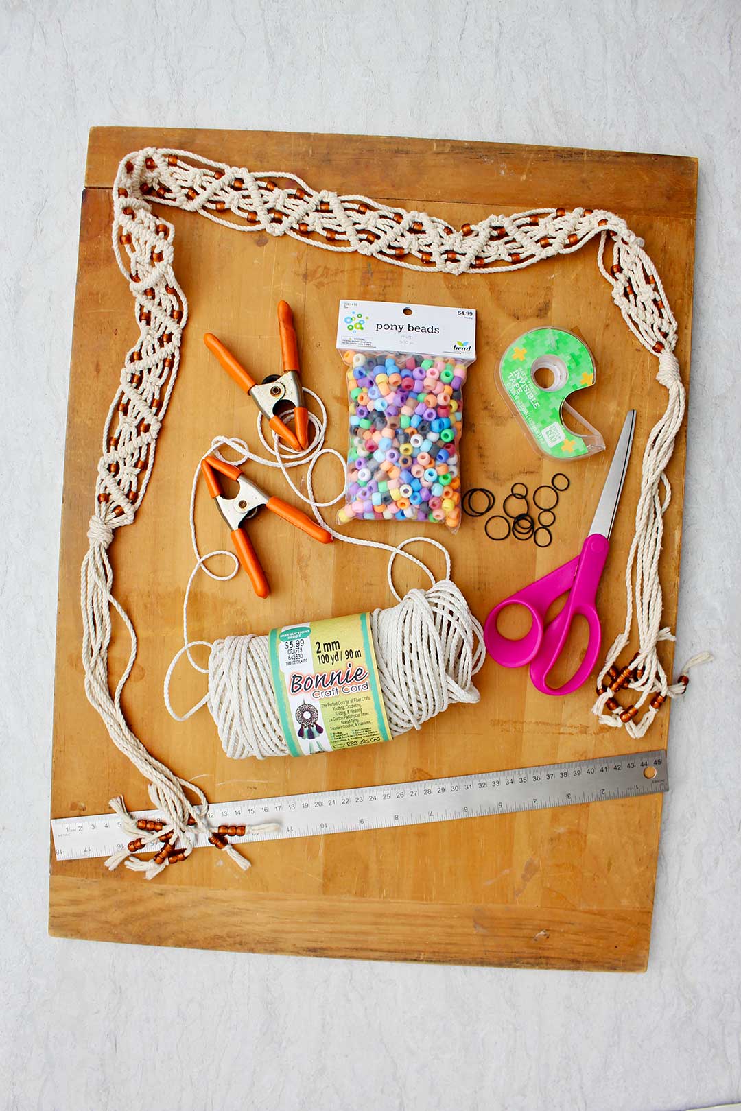 Supplies to make a macrame belt. Colorful beads, clamps, tape, scissors, elastics, a ruler and craft cord.