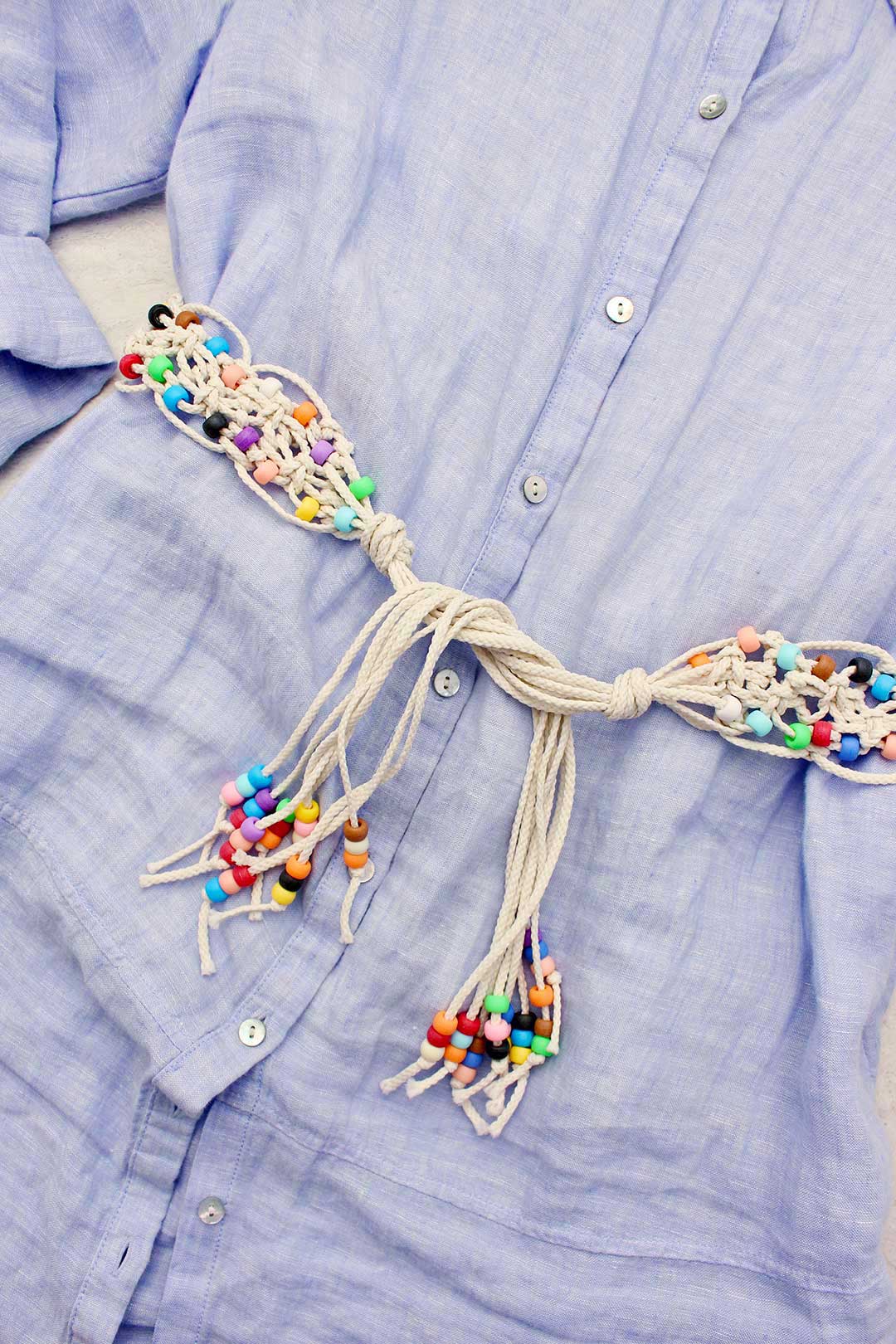 Macrame belt with colorful beads wrapped around blue button down dress.