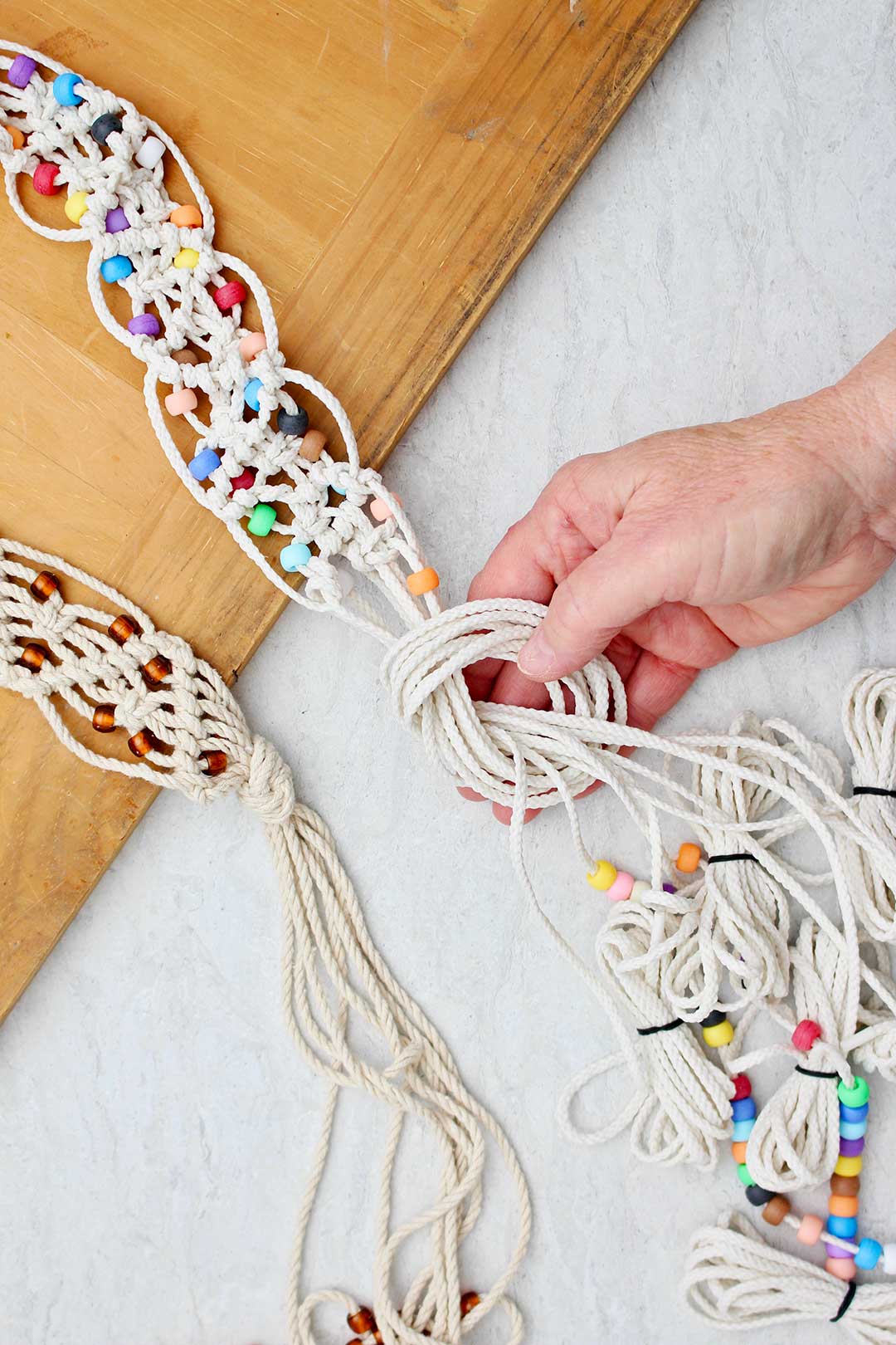 Hand holding loose knot to secure the end of the multi color beaded macrame belt.