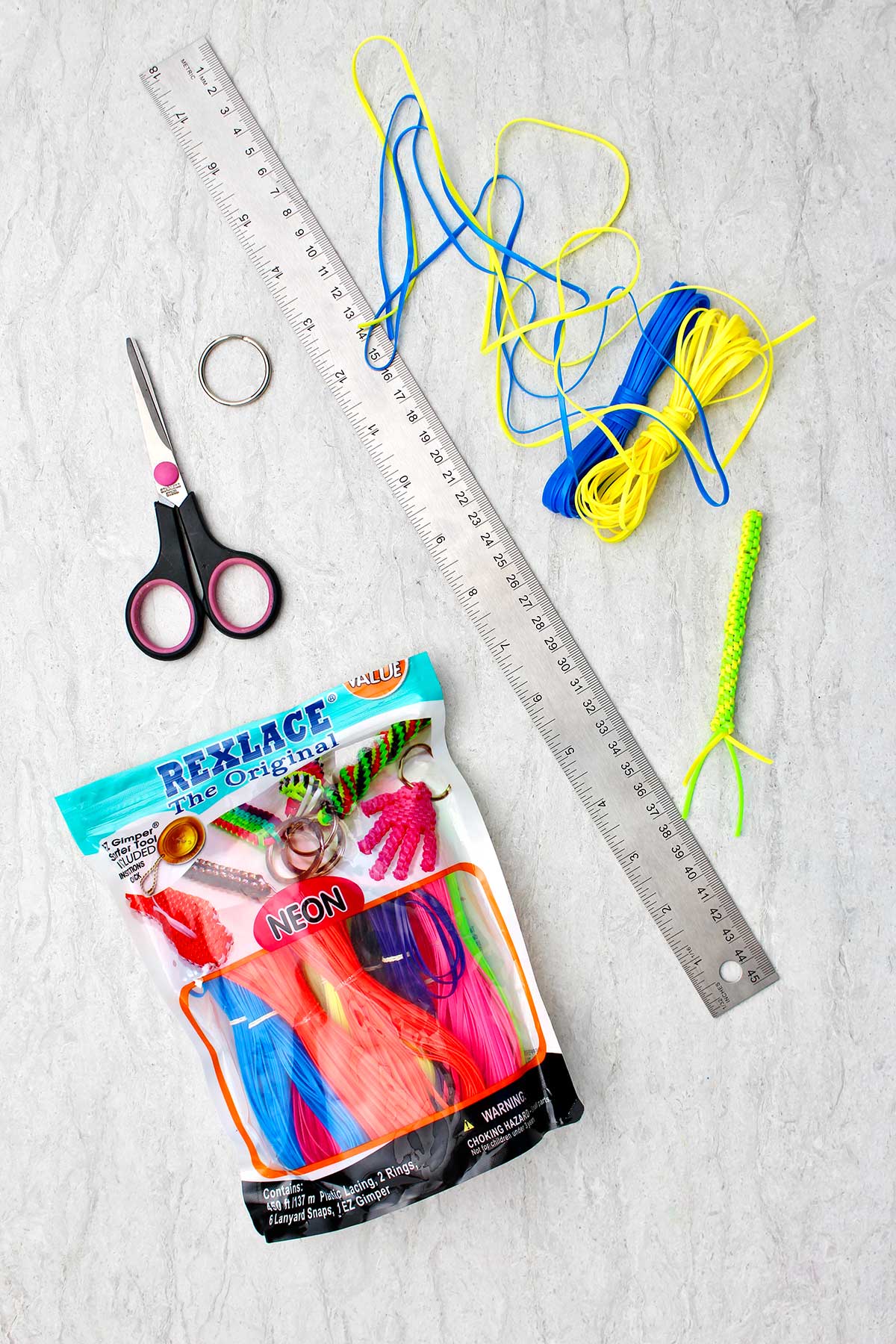 Supplies needed to make a Boondoggle Keychain. Neon Rexlace, scissors, a metal ruler, and a keychain.