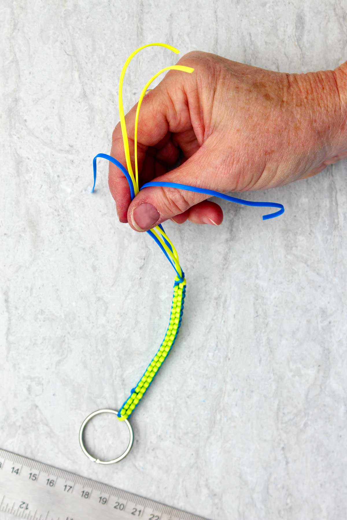 Blue and yellow boondoggle keychain being held at the end by a hand.