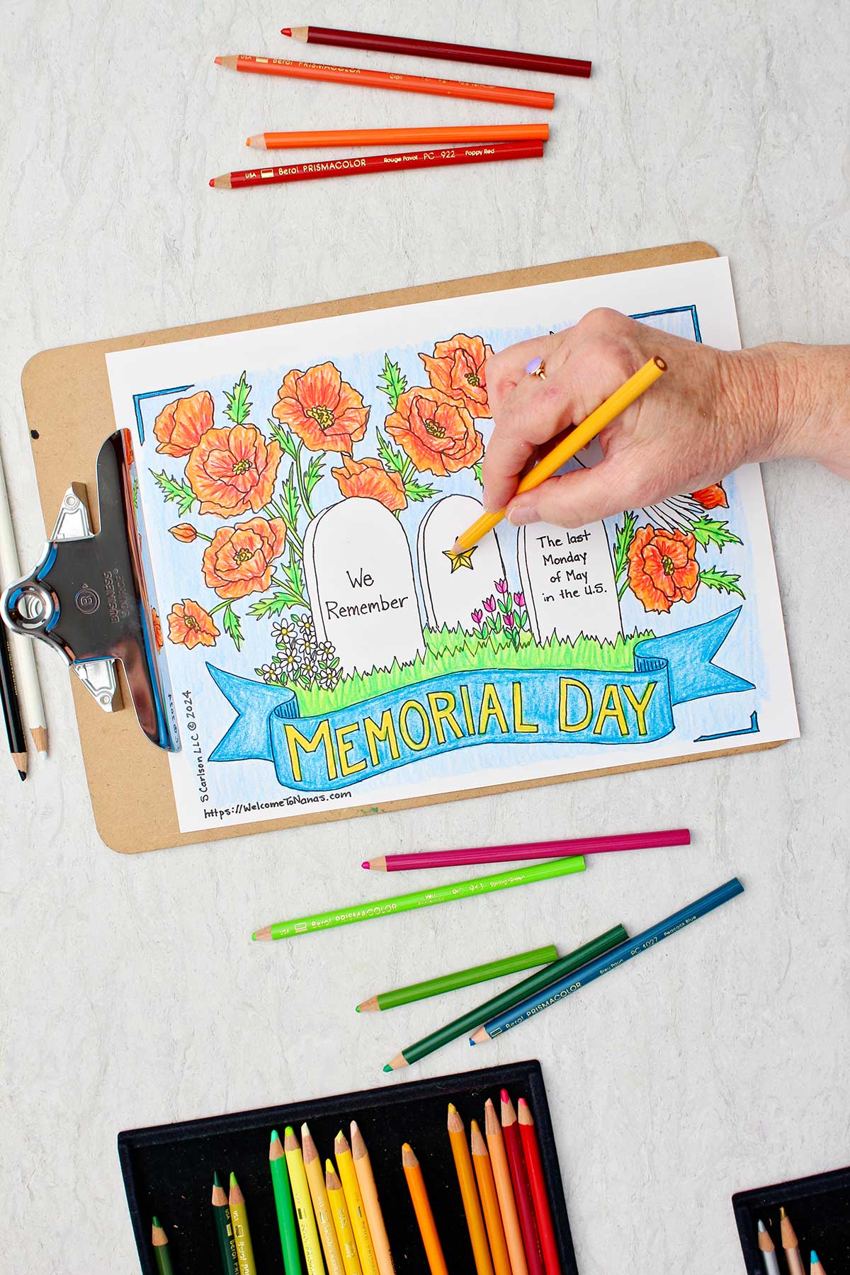 Hand coloring a star on a headstone on Memorial Day Coloring Page yellow with colored pencils near by.