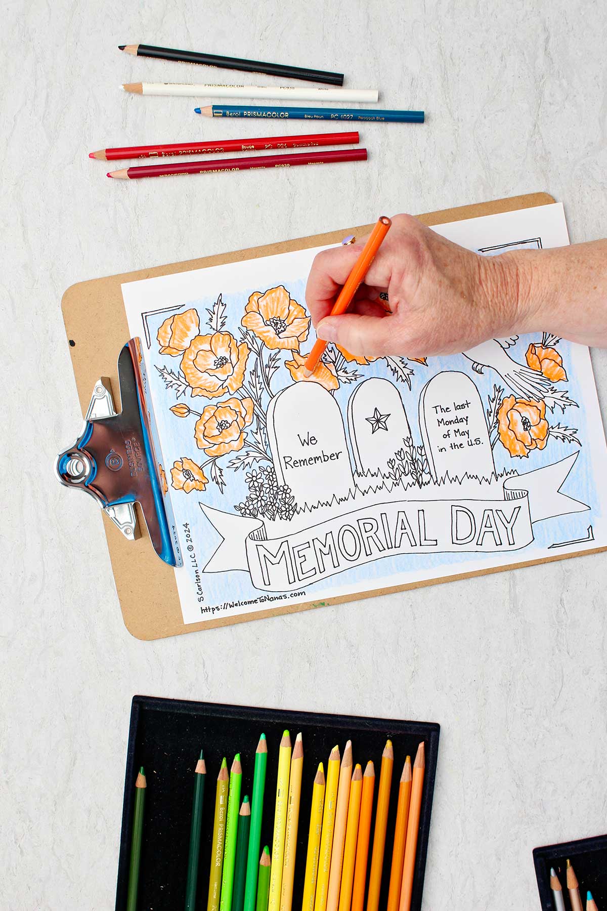 Hand coloring flowers on Memorial Day Coloring page orange with colored pencils near by.